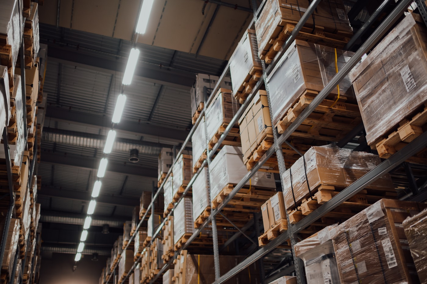 Tall warehouse racking bays stacked with palletised cartons, lit along a receiving aisle.